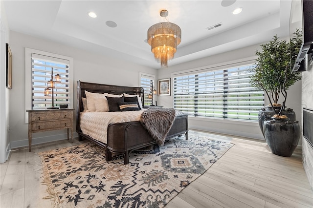 bedroom with a raised ceiling, light hardwood / wood-style floors, and a chandelier