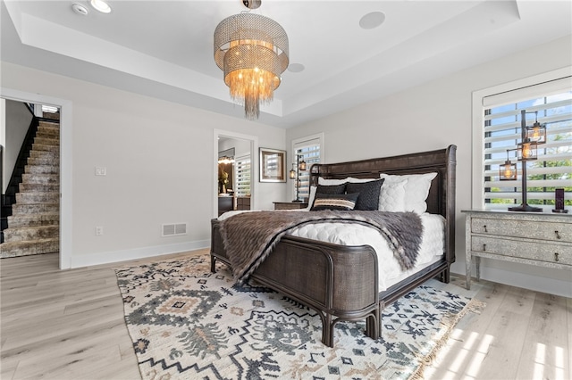 bedroom with light hardwood / wood-style flooring, a tray ceiling, and multiple windows