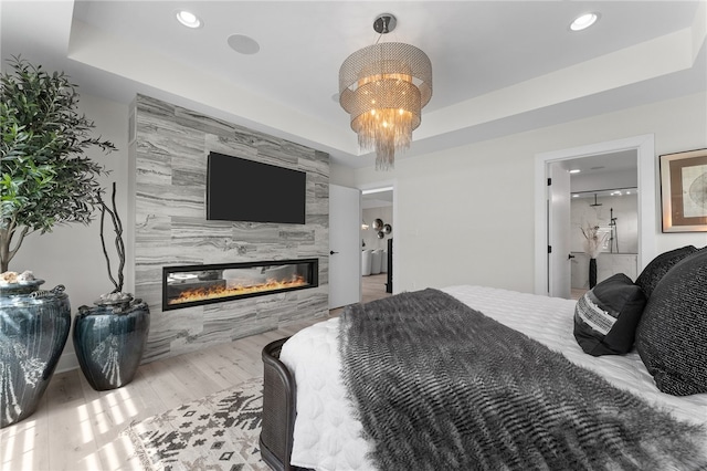 bedroom with light hardwood / wood-style floors, a high end fireplace, a tray ceiling, tile walls, and a notable chandelier