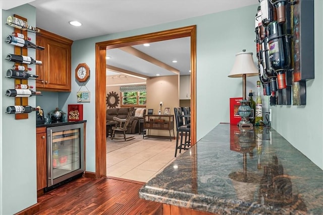 bar with light hardwood / wood-style flooring, beverage cooler, and dark stone countertops