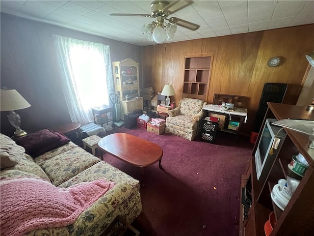 carpeted living room with ceiling fan and wood walls