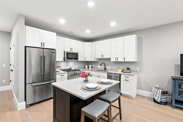 kitchen featuring a sink, light countertops, stainless steel appliances, baseboards, and a kitchen bar