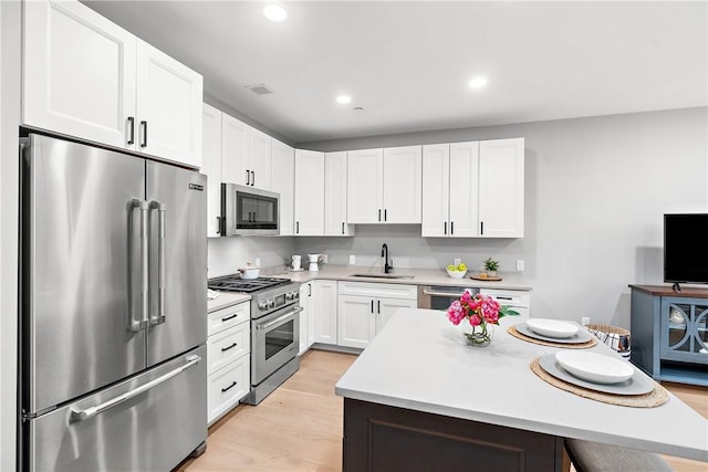 kitchen featuring light countertops, white cabinets, high end appliances, and a sink