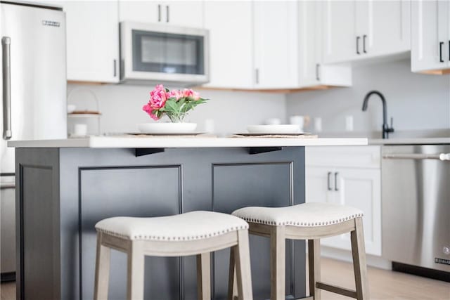 kitchen with stainless steel dishwasher, freestanding refrigerator, white cabinetry, and light countertops