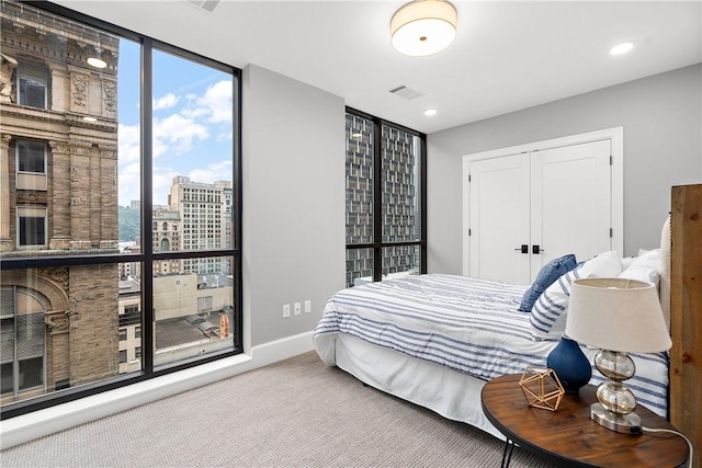 carpeted bedroom with visible vents, a view of city, baseboards, floor to ceiling windows, and a closet