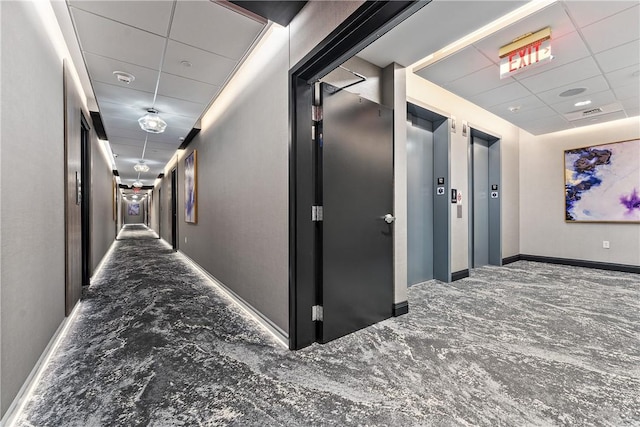 corridor featuring baseboards, a drop ceiling, and elevator