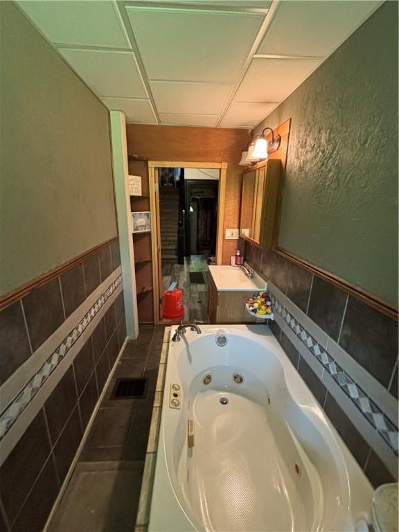 bathroom with a paneled ceiling, tiled tub, and vanity