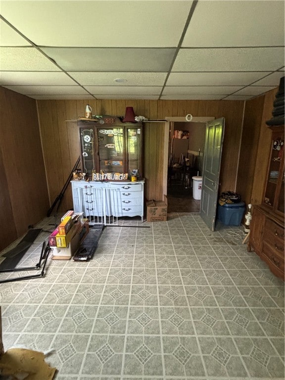 interior space with wood walls, a drop ceiling, and tile patterned floors