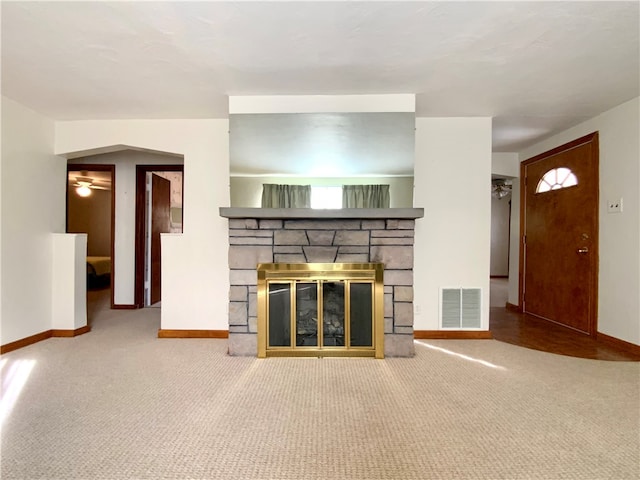 unfurnished living room featuring a stone fireplace, carpet, and ceiling fan