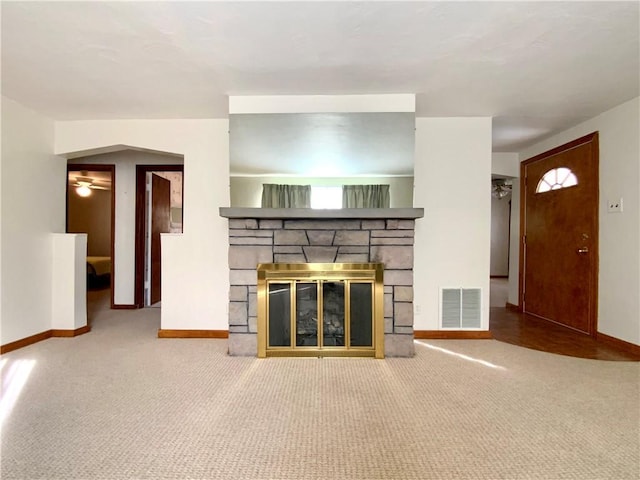 unfurnished living room featuring carpet, visible vents, a stone fireplace, and baseboards