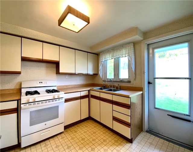 kitchen featuring light tile floors, sink, white gas range oven, and a wealth of natural light