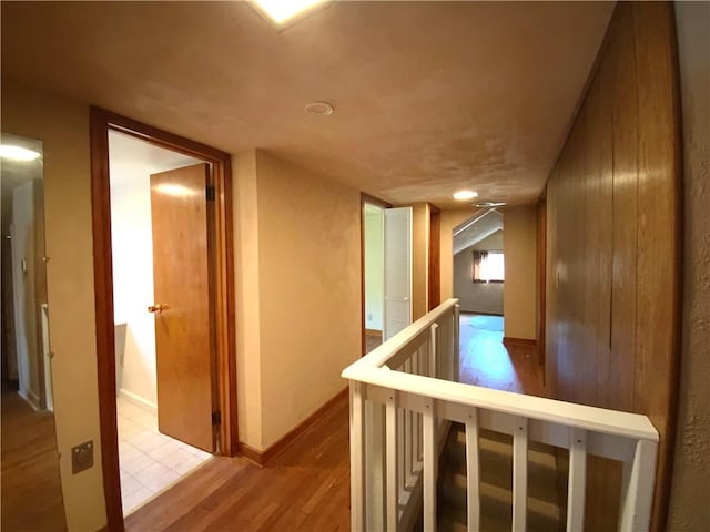 hall with light wood-style floors, baseboards, and an upstairs landing