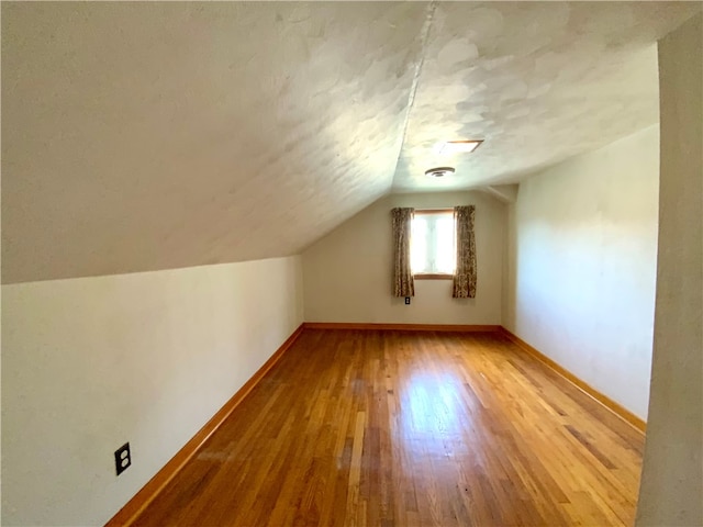 additional living space with a textured ceiling, vaulted ceiling, and hardwood / wood-style floors