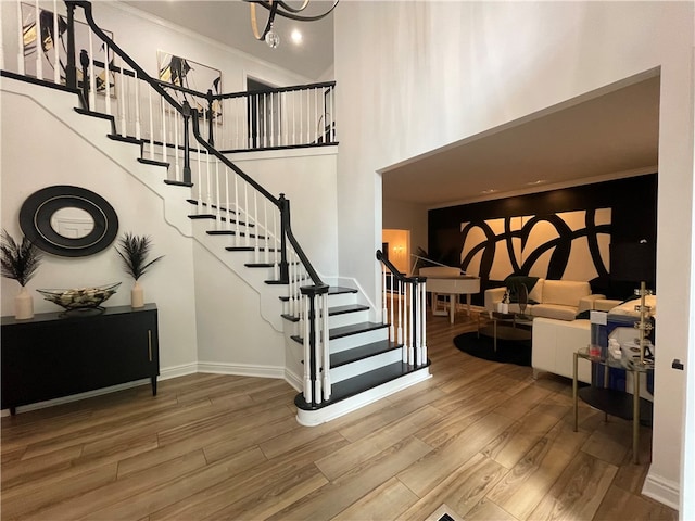 stairway with a high ceiling, ornamental molding, and wood-type flooring