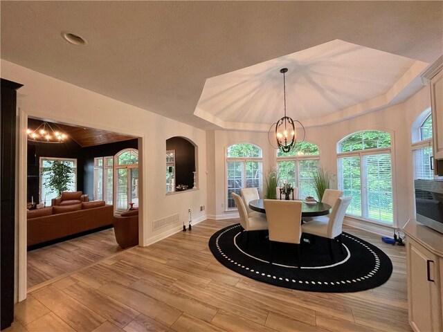 dining room featuring an inviting chandelier, light wood-type flooring, and a raised ceiling