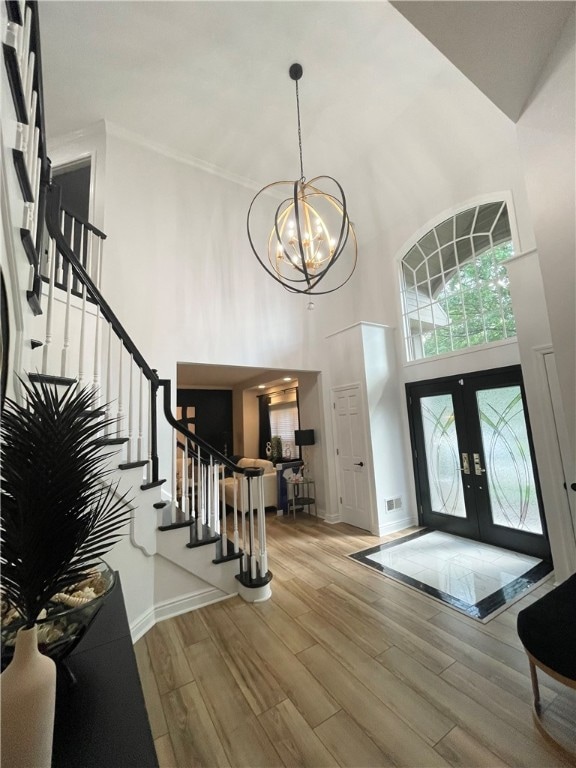 foyer featuring a towering ceiling, hardwood / wood-style flooring, french doors, and an inviting chandelier