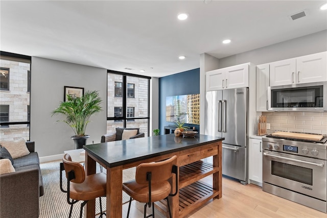 kitchen featuring backsplash, white cabinets, premium appliances, and light wood-type flooring