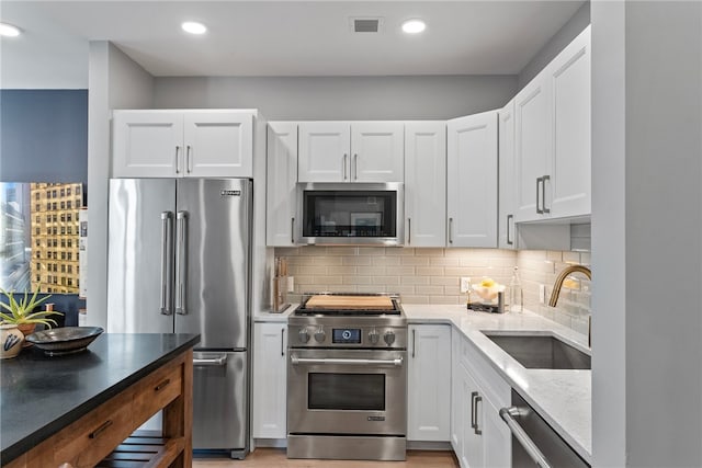 kitchen featuring light wood-type flooring, backsplash, premium appliances, sink, and white cabinetry