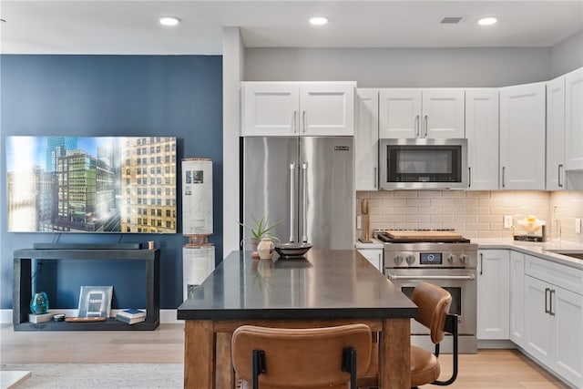 kitchen featuring white cabinetry, light hardwood / wood-style floors, tasteful backsplash, and high quality appliances