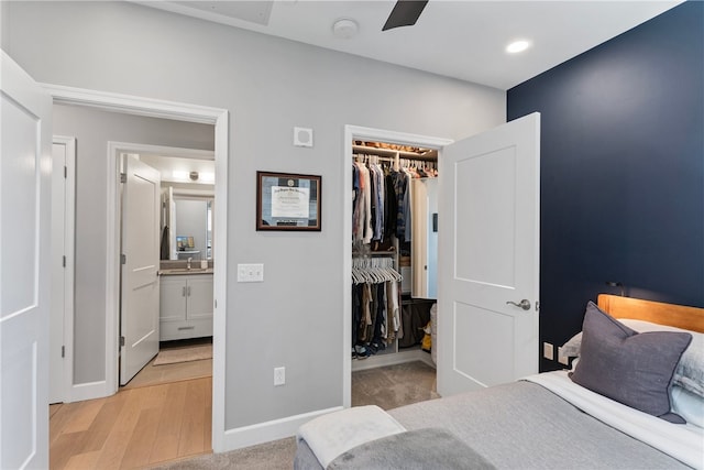 bedroom featuring a closet, light hardwood / wood-style flooring, ceiling fan, connected bathroom, and a spacious closet