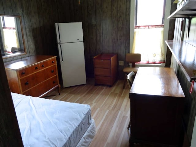 bedroom featuring wooden walls, light wood-type flooring, and white fridge