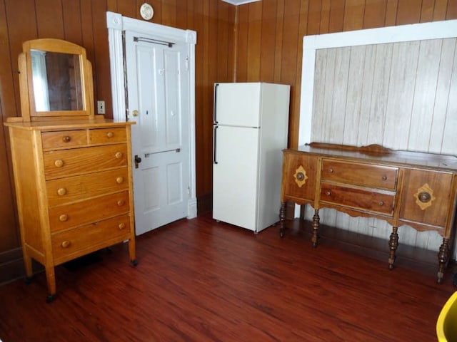 bedroom with dark hardwood / wood-style floors, wood walls, and white fridge