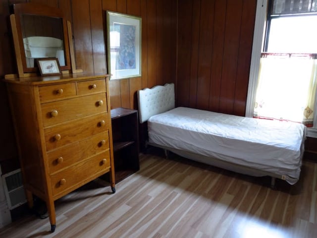 bedroom featuring wood walls, light wood-type flooring, and multiple windows