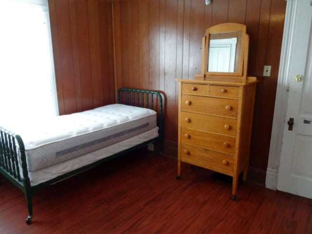 bedroom featuring dark hardwood / wood-style floors, wooden walls, and multiple windows