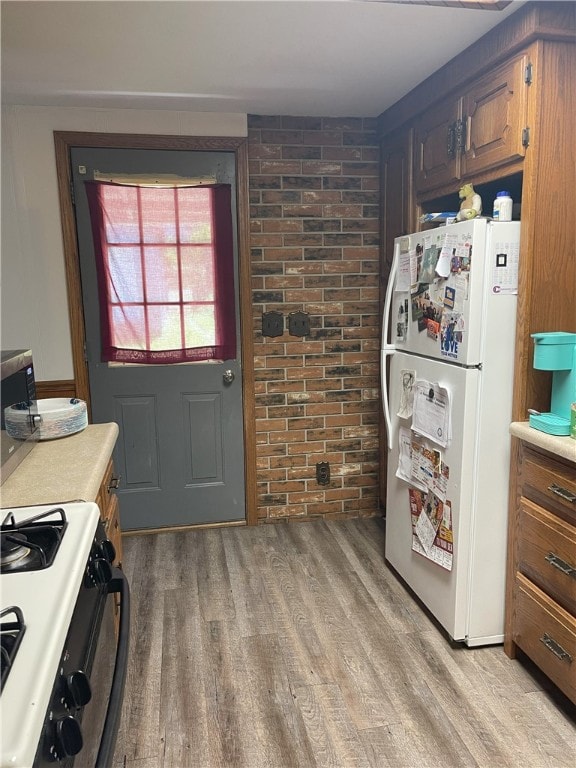 kitchen featuring white refrigerator, brick wall, range with gas stovetop, and light wood-type flooring