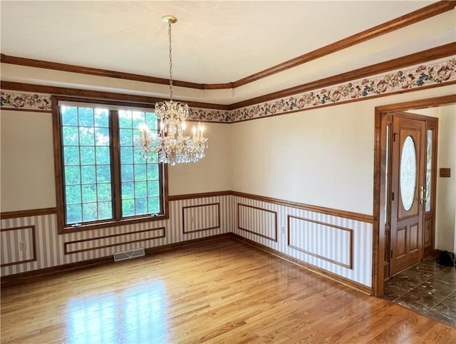 unfurnished room featuring wood-type flooring, crown molding, and a notable chandelier