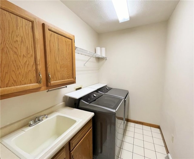 clothes washing area with washer and clothes dryer, cabinets, sink, light tile patterned floors, and a textured ceiling