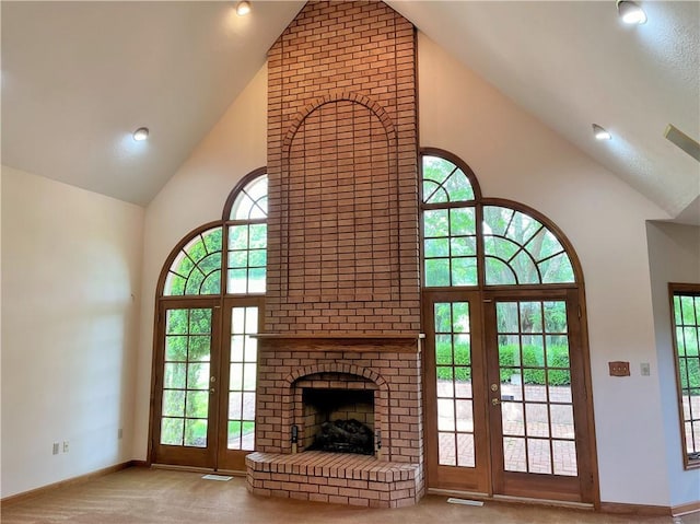 unfurnished living room featuring plenty of natural light, high vaulted ceiling, light colored carpet, and a brick fireplace