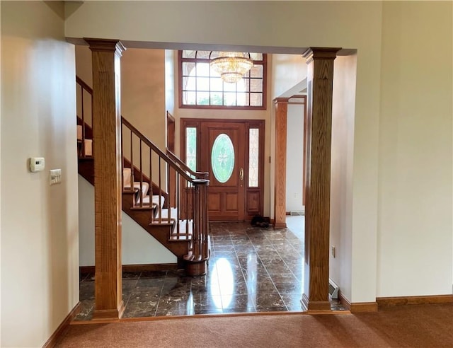 carpeted entryway featuring a towering ceiling, an inviting chandelier, and ornate columns