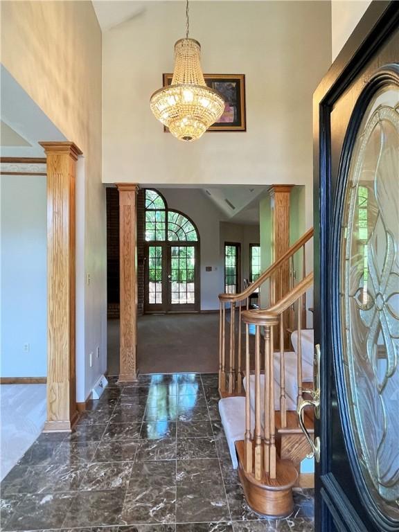 foyer featuring decorative columns, french doors, high vaulted ceiling, and an inviting chandelier