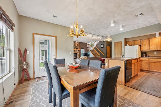 dining area featuring an inviting chandelier, light hardwood / wood-style floors, a stone fireplace, and sink