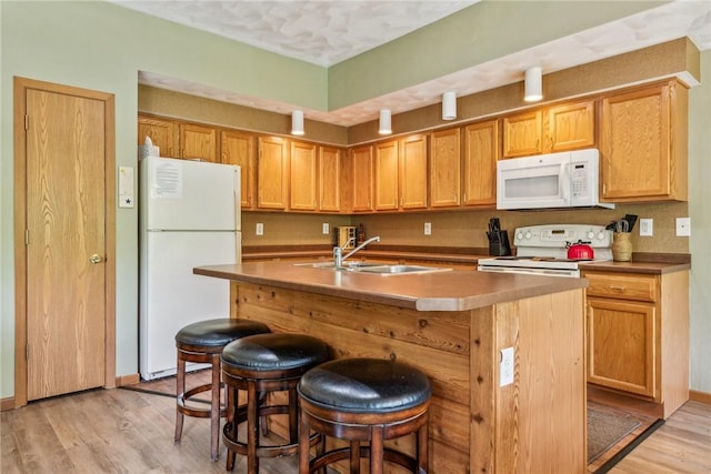 kitchen featuring a kitchen bar, a center island with sink, light hardwood / wood-style floors, white appliances, and sink