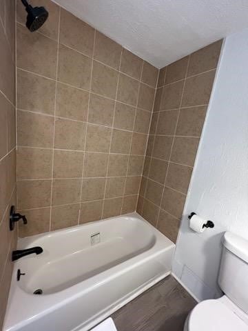 bathroom featuring wood-type flooring, tiled shower / bath, toilet, and a textured ceiling