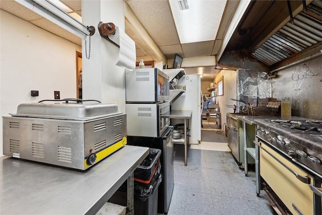 interior space featuring a drop ceiling, stainless steel range with gas stovetop, and white fridge