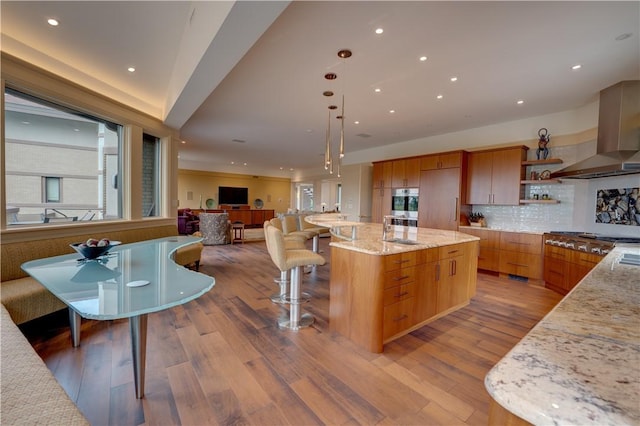 kitchen with backsplash, hardwood / wood-style floors, range hood, a spacious island, and light stone countertops