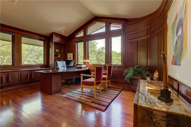 home office featuring vaulted ceiling, hardwood / wood-style floors, and wood walls