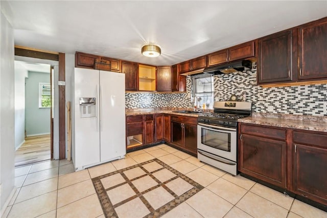 kitchen featuring backsplash, sink, stainless steel gas stove, white fridge with ice dispenser, and light tile patterned floors