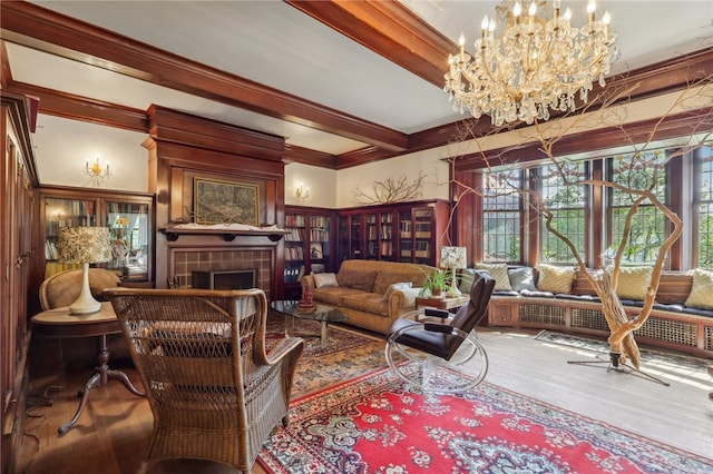 living room featuring hardwood / wood-style floors, beamed ceiling, a fireplace, a notable chandelier, and ornamental molding