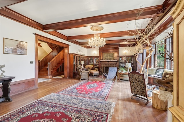 sitting room featuring crown molding, beamed ceiling, a notable chandelier, a tile fireplace, and hardwood / wood-style flooring