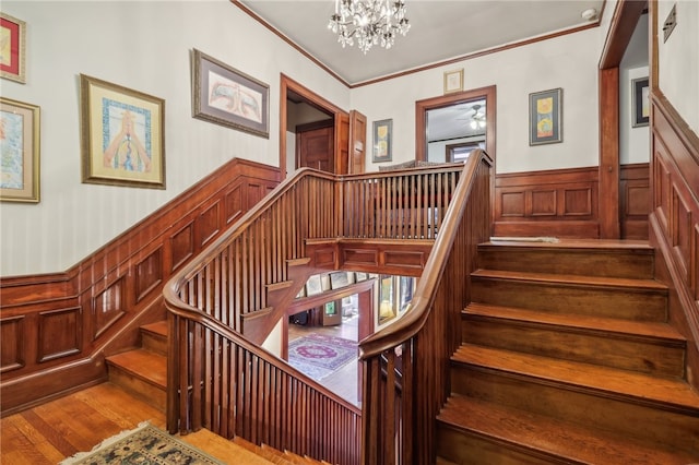 stairs featuring a notable chandelier, wood-type flooring, and crown molding