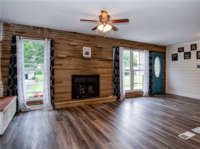 unfurnished living room featuring dark wood-type flooring, wood walls, and plenty of natural light