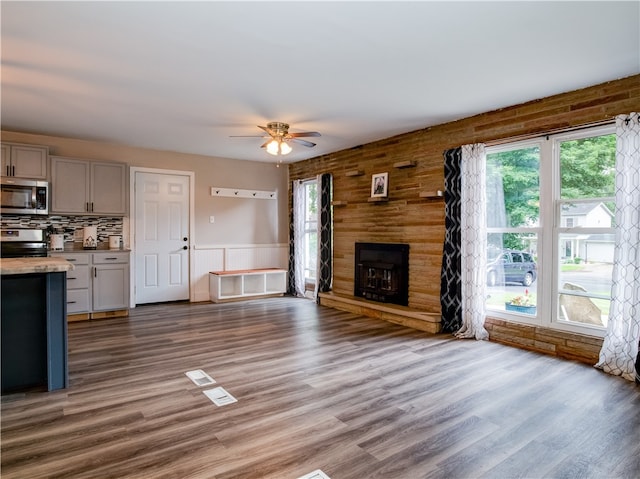 unfurnished living room featuring hardwood / wood-style floors, ceiling fan, a stone fireplace, and wood walls