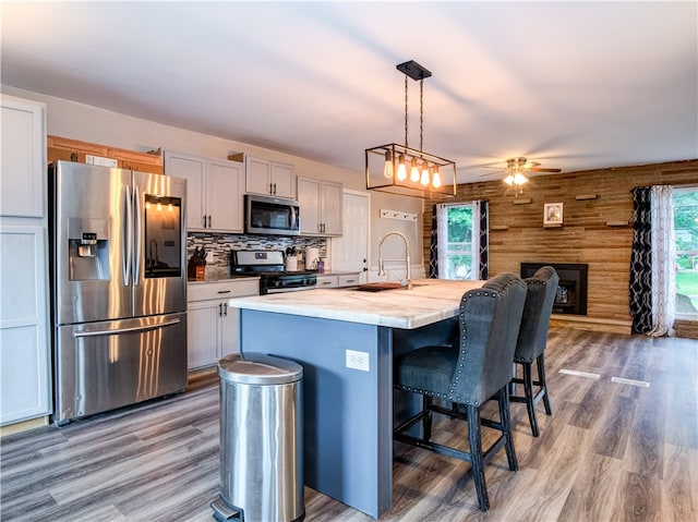 kitchen featuring appliances with stainless steel finishes, white cabinetry, a kitchen island with sink, wooden walls, and sink