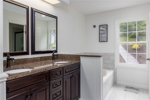 bathroom featuring a relaxing tiled bath, oversized vanity, double sink, and plenty of natural light