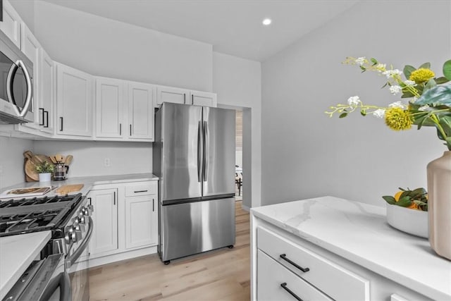 kitchen with light stone countertops, appliances with stainless steel finishes, light hardwood / wood-style flooring, and white cabinetry