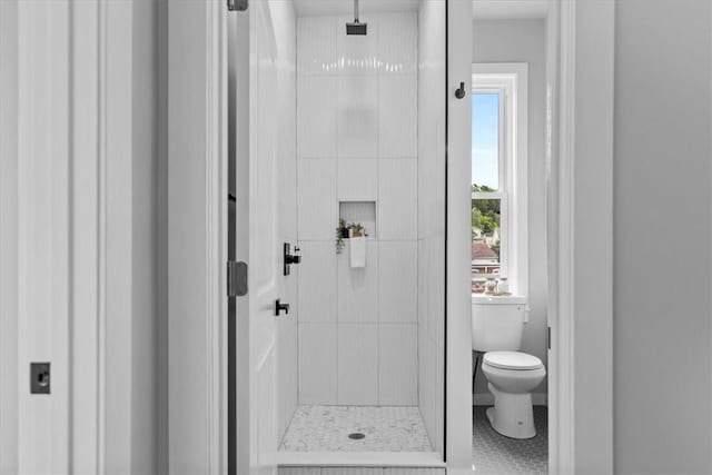 bathroom featuring tile patterned flooring, toilet, and a tile shower